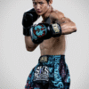 Suablack, a male Muay Thai fighter from Thailand, poses in black SKS Muay Thai gloves with Sakyant design and black SKS Muay Thai shorts with many sakyant patterns, showcasing his athletic build and traditional Thai boxing gear.